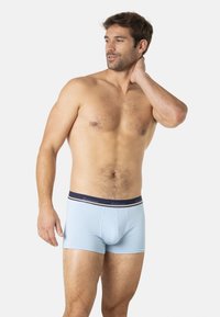 Boxer-briefs pour hommes en bleu clair avec une ceinture navy présentant des accents blancs. Le tissu semble lisse et extensible, offrant un design ajusté.