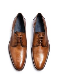 Paar polierte braune Herrenschuhe aus Leder mit Schnürsenkeln, von oben auf weißem Hintergrund betrachtet.