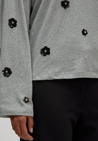 Grijze sweatshirt met lange mouwen, voorzien van zwarte pailletten bloemenappliqués en een relaxte pasvorm, gecombineerd met zwarte broek.