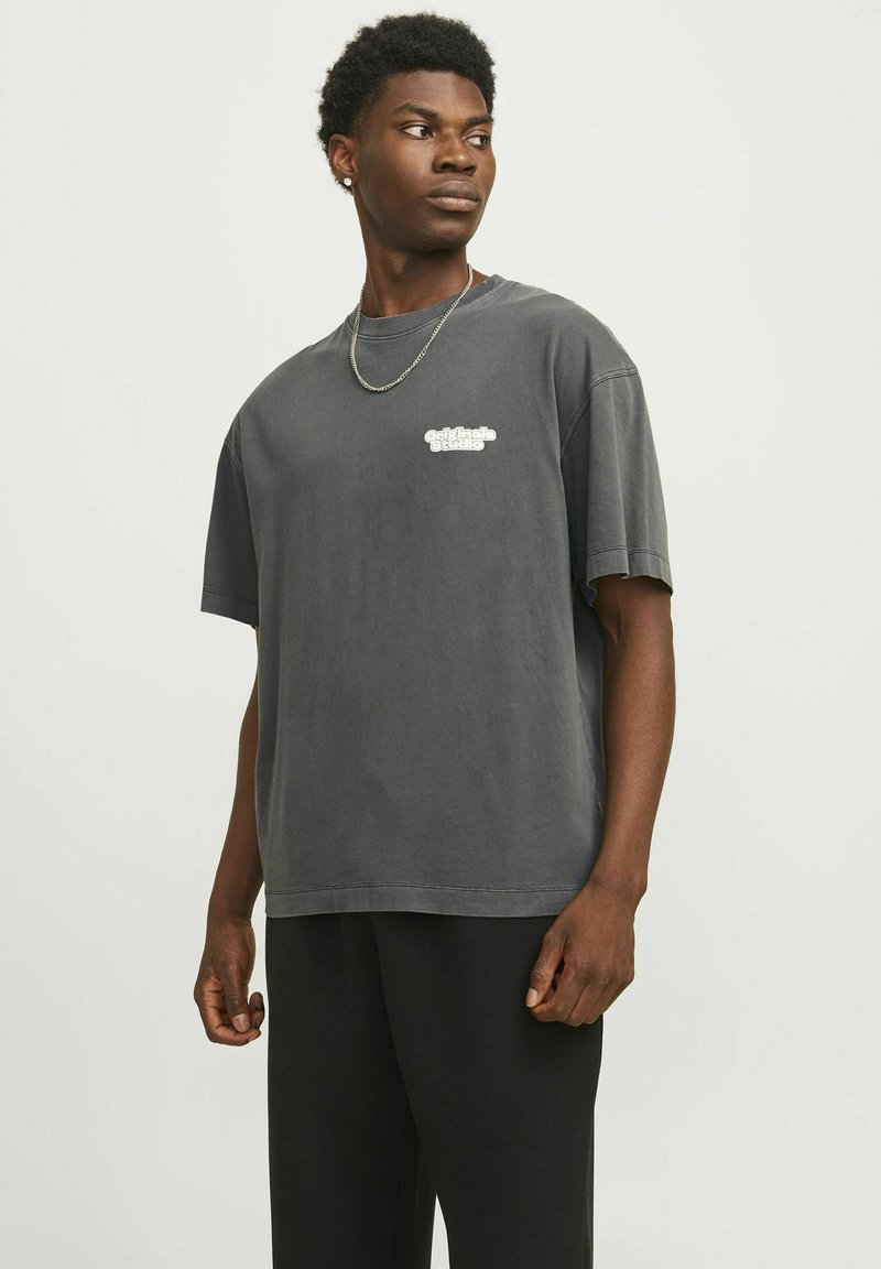 Grå oversized T-shirt med korte ærmer, prydet med et hvidt logo på brystet. Blødt bomuldsstof, afslappet pasform, rund halsudskæring.