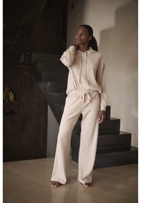 Set di felpa e pantaloni a coste color beige, con cintura regolabile e maniche lunghe, esposto su uno sfondo neutro con scale.