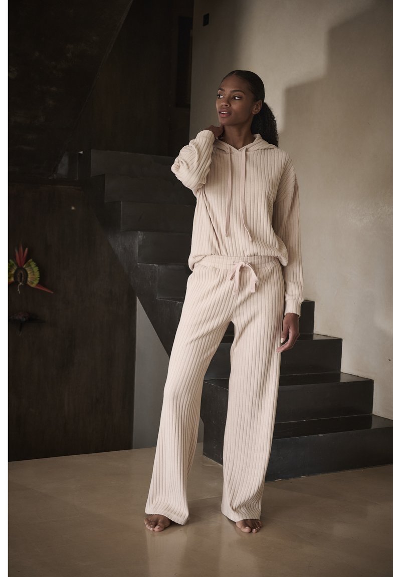 Set di felpa e pantaloni a coste color beige, con cintura regolabile e maniche lunghe, esposto su uno sfondo neutro con scale.