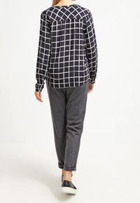 Marineblauwe lange mouwen shirt met een wit ruitpatroon, gecombineerd met grijze joggingbroek. De outfit heeft een losse fit en casual zwarte schoenen.