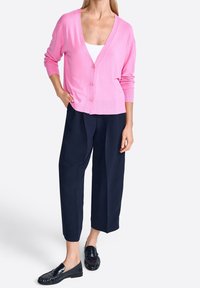 Cardigan en tricot rose avec un décolleté en V profond et cinq boutons, associé à un pantalon large bleu marine et des mocassins noirs.