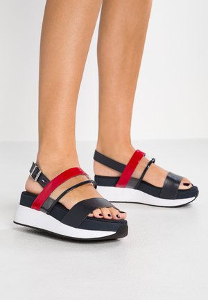 Sort og rød platformsandal med brede remme, tekstureret materiale, åben tå og justerbar ankelspænde. Hvid, gummilignende sål.