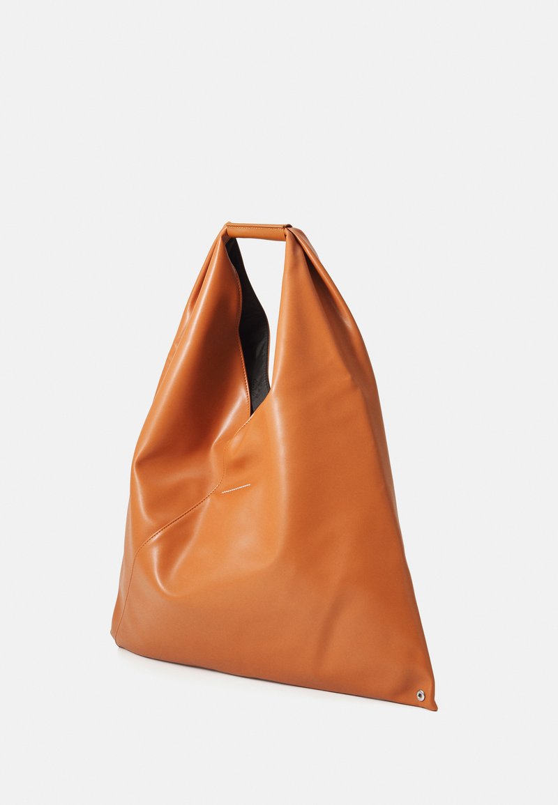 Large soft tan leather tote bag with a folded handle and slightly slouched shape on a white background.