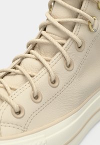 Beige lær sneakers med rund tå, teksturert overflate, gullsnorer og kremfargede lisser. Tykk hvit gummisåle med minimal mønster.