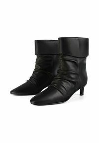 Czarne skórzane botki do połowy łydki z ostrymi noskami, niskimi obcasami typu kitten heel i złożonymi mankietami, wyeksponowane na białym tle.