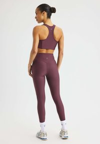 Burgundy atletisk crop-top och leggings i ribbad tyg, med racerback-design och hög midja. Visas i kombination med vita strumpor och sneakers.