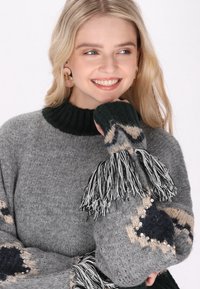 Grau gestrickter Pullover mit einem hohen Kragen, der schwarze und beigefarbene Muster, dekorative Fransen und Perlenakzente an den Ärmeln aufweist.