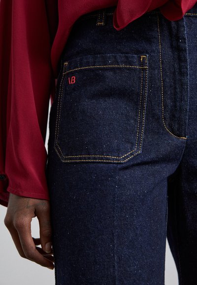 Σκούρο τζιν παντελόνι με στενή εφαρμογή, διακοσμημένο με κόκκινη ραφή λογότυπου στην πίσω τσέπη και κίτρινη αντίθεση ραφής σε όλο το παντελόνι.