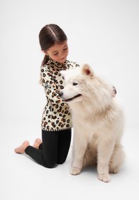 Leopardmönstrad zip-up-topp i beige med orange och svarta detaljer; svarta leggings; vit fluffig Samojedhund. Barn som knäböjer bredvid hunden.