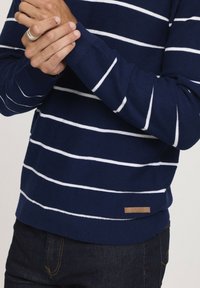 Pull en maille bleu marine rayé avec des rayures horizontales blanches et une étiquette en cuir à l'ourlet.