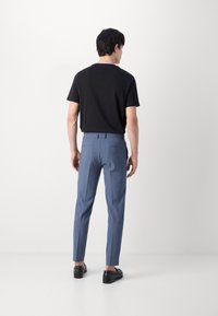 Blå skräddarsydda byxor med smal passform, lättviktsmaterial och rak framdel. Kombinerat med en svart t-shirt med rund halsringning och svarta skor.