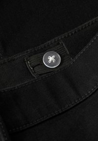 Tissu en denim noir avec une couture plate et une fermeture à bouton, présentant un motif floral blanc sur un bouton transparent. Gros plan sur la texture.