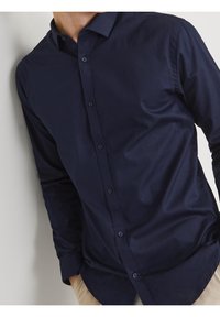 Camisa azul marino de manga larga con botones, textura suave, cuello clásico y cinco botones en la parte delantera. Corte limpio y entallado.