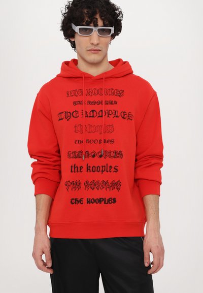 Rode hoodie van katoen met variërende zwarte typografie. Beschikt over een capuchon met trekkoord en ribbelboorden. Gecombineerd met zwarte broek.