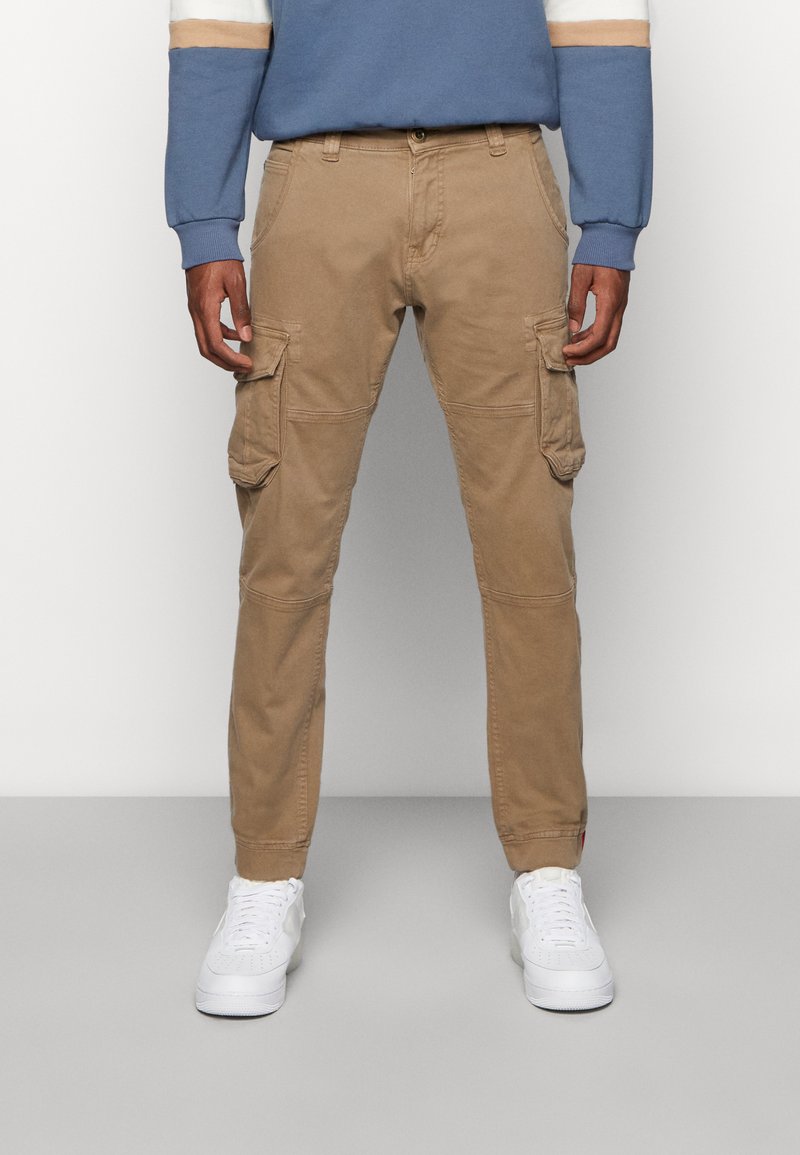 Khakifarbene Cargo-Hosen mit mehreren Seitentaschen, schlanker Schnitt, aus Baumwollmaterial und genähten Details; kombiniert mit weißen Sportschuhen.