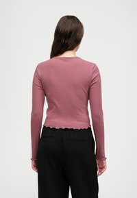 Rebrast pulover z dolgimi rokavi v mauve barvi z zaobljenim ovratnikom in valovitim robom, v kombinaciji z črnimi hlačami s stranskimi žepi.