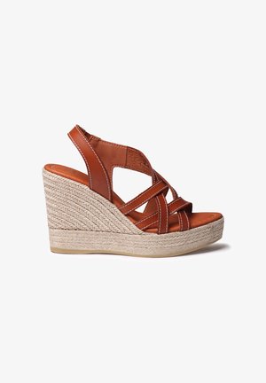Hnedý kožený klinový sandál s prekríženými remienkami, základňou obalenou jutou a textúrovaným povrchom. Má biele prešitie pozdĺž okrajov.