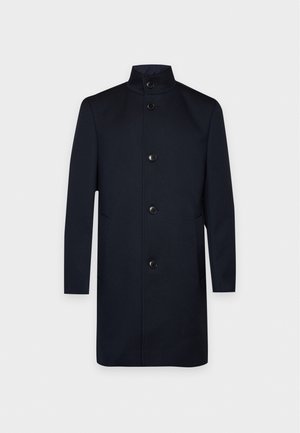 Un manteau pour homme bleu marine foncé, long jusqu’aux genoux, avec un col montant, des manches longues, des boutons devant et des poches latérales, sur un fond uni.