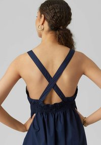 Marinfärgad klänning med korsade axelremmar, elastisk midja med rynk och öppen rygg. Mjuk, lätt tyg med en smidig textur.
