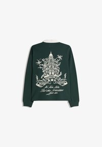 Grøn langærmet skjorte med hvid broderet bygning på bagsiden, med blomsterdetaljer og tekst nederst.