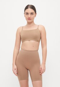 Smeđi bezšavni crop top i šortsevi visokog struka izrađeni od glatkog materijala. Obje komade karakterizira jednostavan dizajn s minimalnim šavovima.