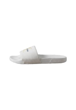 White slide sandal with textured fabric strap and Calvin Klein logo on side and strap, flat sole, open toe design.