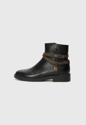 Stivale alla caviglia in pelle nera con suola piatta, caratterizzato da una fascia decorata marrone e dettagli in metallo color oro. Texture liscia.