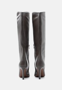 Höga stövlar av mörkgrått läder med klack och bakre blixtlås, visade bakifrån mot en vit bakgrund.