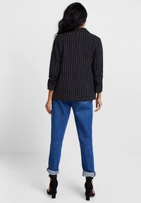 Black shirt with white polka dots, long sleeves, and a collar. Paired with blue denim pants, rolled cuffs, and black high-heeled shoes.