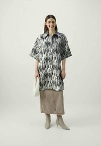 Black and white patterned button-up shirt dress with short sleeves, paired with a beige denim skirt and light gray ankle boots.