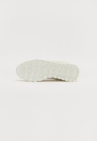 Lichtgekleurde sneakerzool met een gestructureerd patroon van vierkante en rechthoekige grips. Branding zichtbaar nabij de hiel.