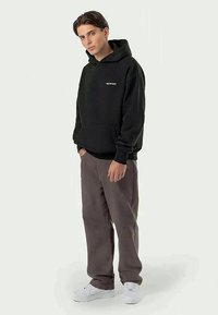 Svart huvtröja med framficka, med en liten logotyp i vitt. Sammanfaller med lösa grå byxor och vita sneakers.