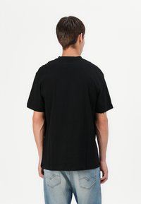 Schwarzes Baumwoll-T-Shirt mit kurzen Ärmeln, lockerer Passform, rundem Ausschnitt und ohne sichtbares Logo. Kombiniert mit hellblauen Jeans.