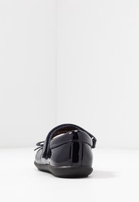 Granatowe baleriny z lakierowanej skóry z zaokrąglonym czubkiem, ozdobione teksturowanym materiałem z tyłu oraz małą kokardką z przodu. Płaska, elastyczna podeszwa.