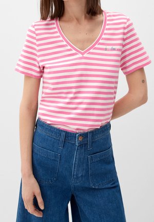 Kobieta w różowo-białej pasiastym T-shircie z dekoltem w serek z napisem „joyful.” oraz niebieskich wysokich dżinsach z kieszeniami z przodu.