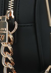 Borsa a mano nera in pelle sintetica con cerniera in tonalità oro, dettaglio a catena e accenti metallici. Il materiale ha una texture liscia con linee cucite.