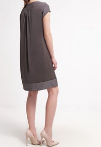 Vestido corto gris de manga corta con la parte posterior plizada, dobladillo gris sólido y textura suave, combinado con zapatos de tacón nude.