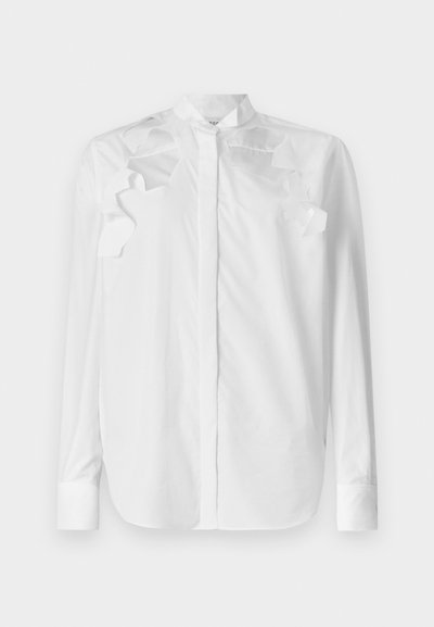 White long-sleeve shirt in cotton with a mandarin collar. Features layered ruffle accents on the shoulders and button closure at the front.
