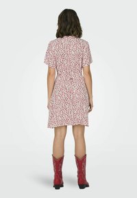Short-sleeve dress in light pink with a floral pattern; fitted waist with a tie, knee-length. Paired with red cowboy boots featuring stitching details.