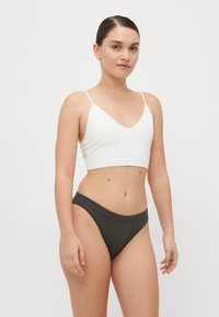 Witte katoenen bralette met spaghettibandjes en een V-hals, gecombineerd met olijfgroene high-waisted slipjes. Vrouwelijke textuur, minimalistisch design.