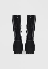 Botas negras de media pantorrilla con tacones gruesos y cremalleras traseras, que presentan paneles de cuero liso y texturizado con un patrón de cocodrilo en la parte superior.