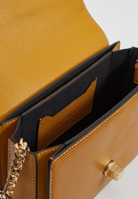 Borsa a tracolla in pelle gialla testurizzata con interno nero, dotata di scomparti per carte di credito e chiusura in hardware dorato.