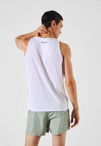 Canotta bianca senza maniche con scollatura rotonda, caratterizzata da un logo del marchio sul retro. Abbinata a pantaloni corti verdi chiari, che mostrano una vestibilità casual.