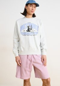 Gray sweatshirt with "DETROIT CARHARTT WIP" graphic in blue, paired with pink shorts. The sweatshirt is casual and ribbed at the cuffs.