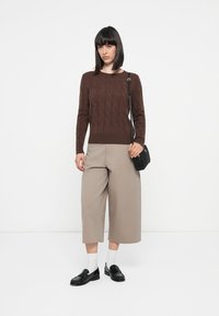 Brown cable-knit sweater, beige wide-leg trousers, white socks, black loafers, and a small black crossbody bag. Simple, modern design.