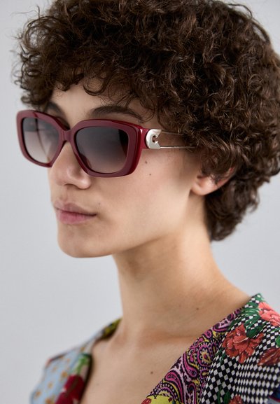 Lunettes de soleil carrées surdimensionnées rouges avec des verres dégradés, accent argenté sur les branches et monture en plastique brillant.