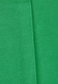 Tessuto a maglia verde con una trama liscia, caratterizzato da un motivo uniforme e una leggera costina. Due pezzi che si intersecano ad un angolo.